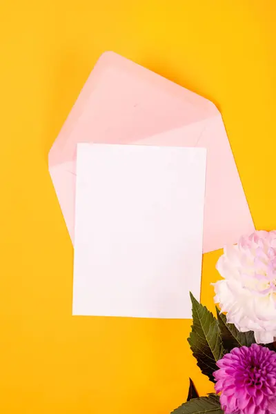 黄色の背景にピンクの封筒と白と紫色のディアリアスの花とブランクの挨拶カードモックアップ コピースペースでブランク招待状またはグリーティングカードモックアップ ストック写真