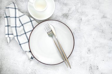 Temiz beyaz bir tabak, düzgün yerleştirilmiş çatal bıçak takımı ve minimalist bir bardak içeren basit ama zarif bir masa düzenlemesi., 