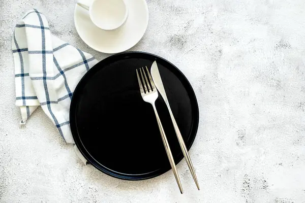 Siyah tabak, çatal bıçak takımı ve beyaz bardaklı minimalist masa. Yemek fotoğrafçılığı ve restoran pazarlaması için mükemmel., 