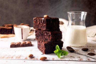 Eritilmiş çikolata soslu çikolatalı kek, badem ve masada bir bardak sütle naneli yaprak. Fırın, şekerleme konsepti