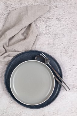 Masada iki boş seramik gri tabak, çatal bıçak takımı ve beyaz masada bir peçete var. Tarafsız renkler. 