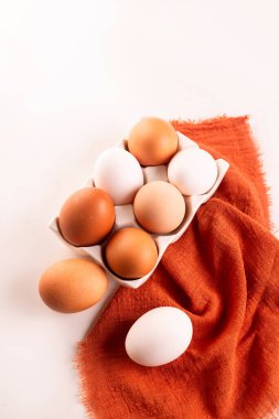 Çiğ kahverengi ve beyaz tavuk yumurtalarını turuncu keten peçeteye sarıp yumurta kasasına koy..