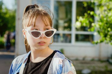 Mavi baskılı gömlekli ve retro güneş gözlüklü modacı kız kameraya özgüvenle bakıyor..