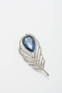 Metalik altın broş tüy şeklinde, parlak mavi değerli taş taklidi, beyaz arka planda iğne, bijouterie, yakın takı