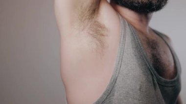 Close up slow motion shoot of sweaty and smelly from heat man touching his hairy armpit. Removal of unwanted hair, using of deodorant or antiperspirant from sweat and smell. Beauty standards, bodypositive concept.