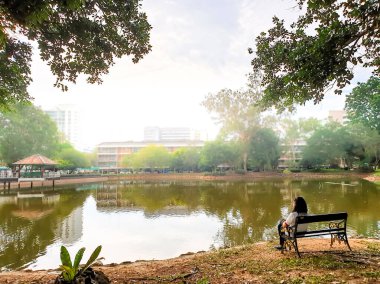Parktaki gölette tek başına oturan Asyalı kadın.