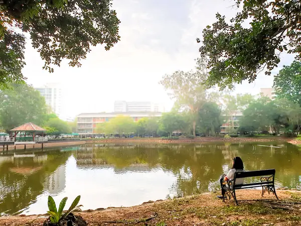 Parktaki gölette tek başına oturan Asyalı kadın.