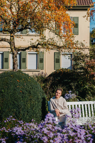 a girl sits on a bench in the park and enjoys the sun. Portrait young adult attractive woman enjoy sitting on bench and relaxing calm carefree rest in city park against green grass and trees on sunny