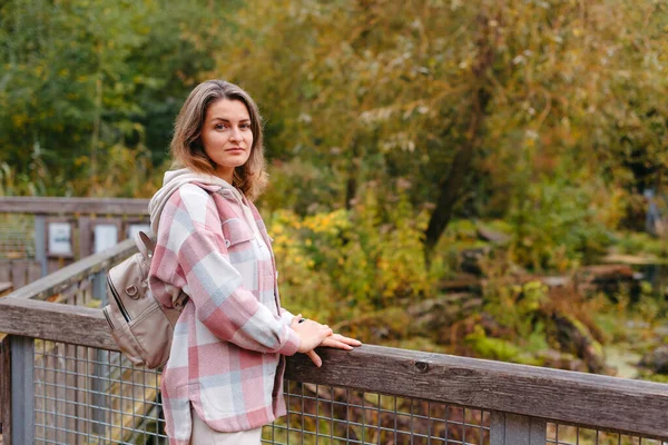 秋天里穿着休闲装 站在秋天里公园和河边桥上的可爱年轻女子的画像 金秋时在公园散步的漂亮女人 复制空间 笑着的女孩 — 图库照片