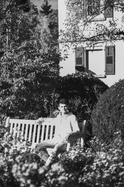 一个青少年坐在公园的长椅上 一边喝着热杯子里的咖啡 一边看手机 — 图库照片