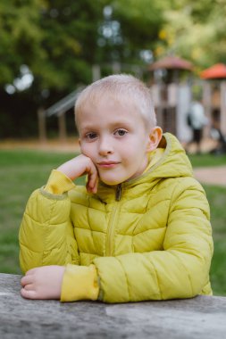 Sonbahar mevsiminde bir çocuk parkta bir masada oturur. Sonbahar parkında, ahşap bankta ve masada oturan çocuk. Dışarıdaki Küçük Çocuk