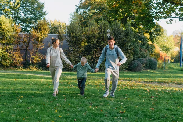 a family mom and 2 sons are having fun, running in the park and jumping. Sons, children, mom, run, play, rejoice, enjoy nature in summer. Family teamwork. Happy family team, running together in field
