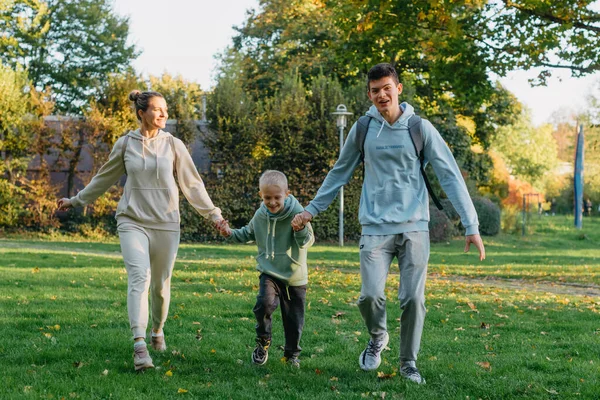 a family mom and 2 sons are having fun, running in the park and jumping. Sons, children, mom, run, play, rejoice, enjoy nature in summer. Family teamwork. Happy family team, running together in field