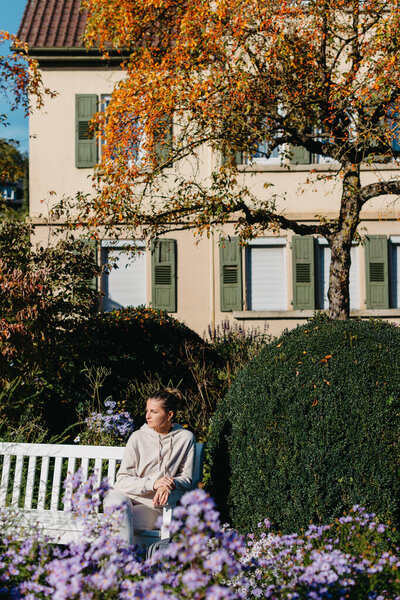 a girl sits on a bench in the park and enjoys the sun. Portrait young adult attractive woman enjoy sitting on bench and relaxing calm carefree rest in city park against green grass and trees on sunny