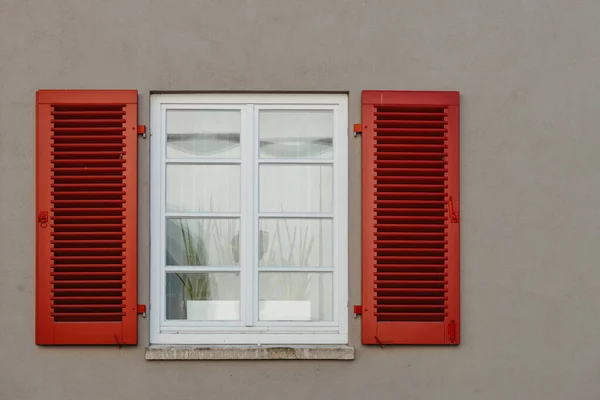 Italian windows on the white wall facade with open red color classic shutters and flowers on the windows. window shutter wall