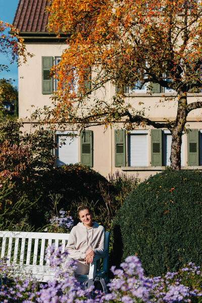 a girl sits on a bench in the park and enjoys the sun. Portrait young adult attractive woman enjoy sitting on bench and relaxing calm carefree rest in city park against green grass and trees on sunny