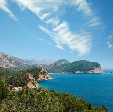 Denizden güneşli bir günde kayaların üzerinde resim gibi bir manzara. Budva Riviera, Karadağ. Karadağ 'ın Budva adası Sveti Nikola' nın hava manzarası. Hawaii plajı, şemsiyeler, banyolar ve kristal berrak sular