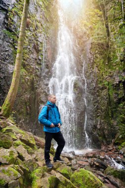 Almanya 'nın turistik merkezi - Schapbach yakınlarındaki Burgbach Şelalesi, Kara Orman, Baden-Wurttemberg, Almanya. Mavi ceketli bir adam taşın üzerinde duruyor ve düşen suyun akışına bakıyor.