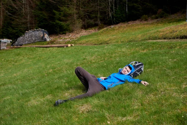 Tired hiker in blue resting lying and relaxing on the top of a high mountain. Hiker resting lying on the grass in a valley of a high mountain