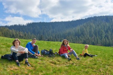 Parktaki çimlerin üzerinde oturan mutlu bir aile. Mutlu bir genç aile yaz günü dışarıda vakit geçirir.