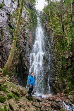 Almanya 'nın turistik merkezi - Schapbach yakınlarındaki Burgbach Şelalesi, Kara Orman, Baden-Wurttemberg, Almanya. Mavi ceketli bir adam taşın üzerinde duruyor ve düşen suyun akışına bakıyor.