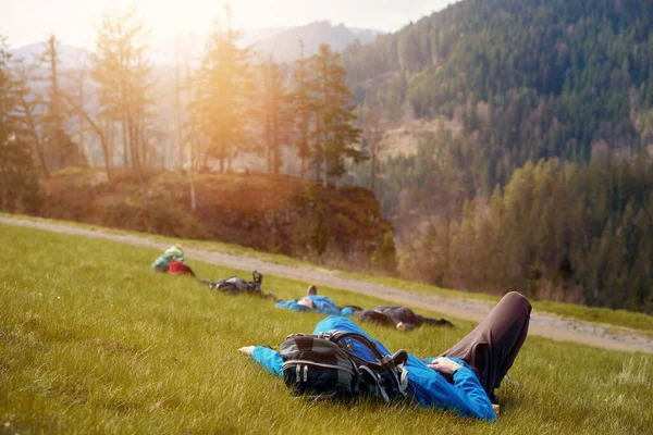 Tired hiker in blue resting lying and relaxing on the top of a high mountain. Hiker resting lying on the grass in a valley of a high mountain