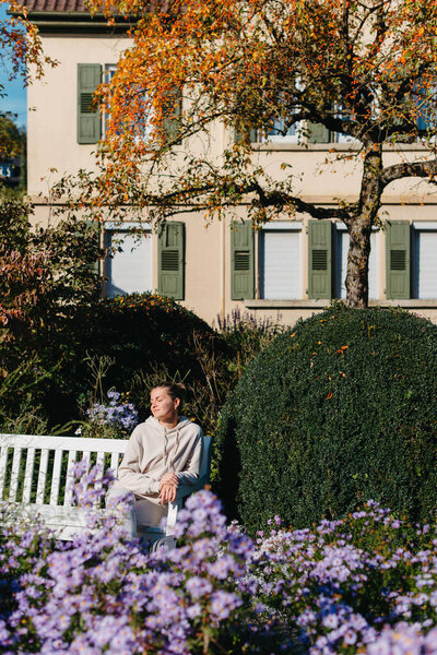 a girl sits on a bench in the park and enjoys the sun. Portrait young adult attractive woman enjoy sitting on bench and relaxing calm carefree rest in city park against green grass and trees on sunny