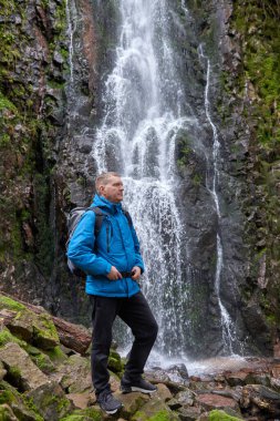 Almanya 'nın turistik merkezi - Schapbach yakınlarındaki Burgbach Şelalesi, Kara Orman, Baden-Wurttemberg, Almanya. Mavi ceketli bir adam taşın üzerinde duruyor ve düşen suyun akışına bakıyor.