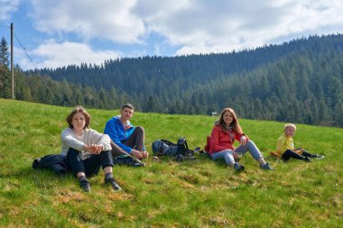 Parktaki çimlerin üzerinde oturan mutlu bir aile. Mutlu bir genç aile yaz günü dışarıda vakit geçirir.