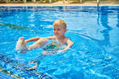 Küçük bir çocuk, sekiz yaşında, havuzda su sıçratıyor, eğlenceli aktiviteler yapıyor. Çocuk havuzda yüzmekten mutlu. Havuzda etkinlikler, yüzen ve suda oynayan çocuklar, mutluluk ve...