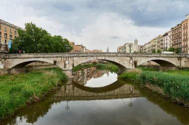 Renkli sarı ve turuncu evler ve Pont de Sant Agusti köprüsü Girona, Katalonya, İspanya 'daki Onyar su nehrine yansıdı. Arka planda Sant Feliu Kilisesi ve Saint Mary Katedrali. 