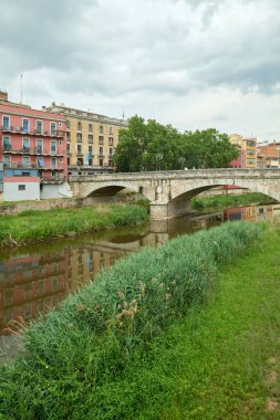 Renkli sarı ve turuncu evler ve Pont de Sant Agusti köprüsü Girona, Katalonya, İspanya 'daki Onyar su nehrine yansıdı. Arka planda Sant Feliu Kilisesi ve Saint Mary Katedrali. 