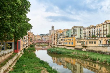 Eski Girona, Katalonya, İspanya ve Avrupa 'nın manzarası. Yaz gezisi. Renkli sarı ve turuncu evler ve Pont de Sant Agusti köprüsü Girona, Katalonya, İspanya 'daki Onyar su nehrine yansıdı. Kilise