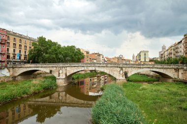 Renkli sarı ve turuncu evler ve Pont de Sant Agusti köprüsü Girona, Katalonya, İspanya 'daki Onyar su nehrine yansıdı. Arka planda Sant Feliu Kilisesi ve Saint Mary Katedrali. 