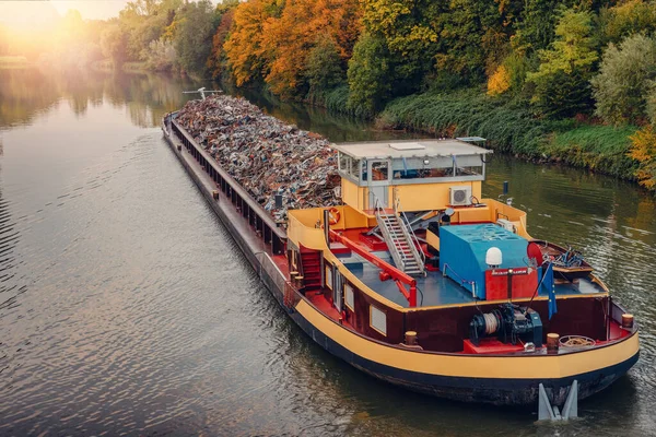 Transportation industry. Ship barge transports scrap metal and sand with gravel. Barge loaded with scrap metal is on the roadstead. Scrap metal transportation by water. Barge laden by metal salvage
