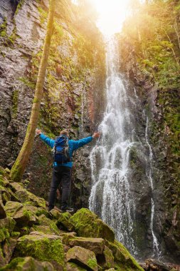 Almanya 'nın turistik merkezi - Schapbach yakınlarındaki Burgbach Şelalesi, Kara Orman, Baden-Wurttemberg, Almanya. Mavi ceketli bir adam taşın üzerinde duruyor ve düşen suyun akışına bakıyor.