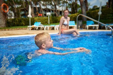 Küçük bir çocuk, sekiz yaşında, havuzda su sıçratıyor, eğlenceli aktiviteler yapıyor. Çocuk havuzda yüzmekten mutlu. Havuzda etkinlikler, yüzen ve suda oynayan çocuklar, mutluluk ve...
