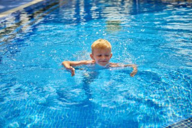 Küçük bir çocuk, sekiz yaşında, havuzda su sıçratıyor, eğlenceli aktiviteler yapıyor. Çocuk havuzda yüzmekten mutlu. Havuzda etkinlikler, yüzen ve suda oynayan çocuklar, mutluluk ve...