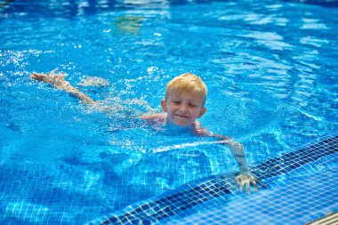 Küçük bir çocuk, sekiz yaşında, havuzda su sıçratıyor, eğlenceli aktiviteler yapıyor. Çocuk havuzda yüzmekten mutlu. Havuzda etkinlikler, yüzen ve suda oynayan çocuklar, mutluluk ve...