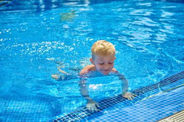 Küçük bir çocuk, sekiz yaşında, havuzda su sıçratıyor, eğlenceli aktiviteler yapıyor. Çocuk havuzda yüzmekten mutlu. Havuzda etkinlikler, yüzen ve suda oynayan çocuklar, mutluluk ve...