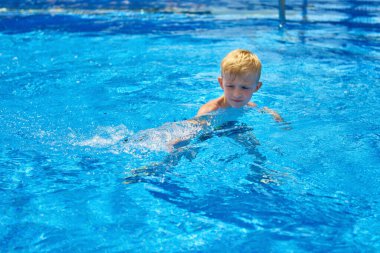 Küçük bir çocuk, sekiz yaşında, havuzda su sıçratıyor, eğlenceli aktiviteler yapıyor. Çocuk havuzda yüzmekten mutlu. Havuzda etkinlikler, yüzen ve suda oynayan çocuklar, mutluluk ve...