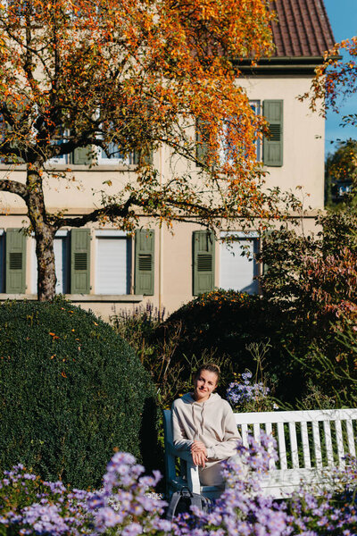 a girl sits on a bench in the park and enjoys the sun. Portrait young adult attractive woman enjoy sitting on bench and relaxing calm carefree rest in city park against green grass and trees on sunny