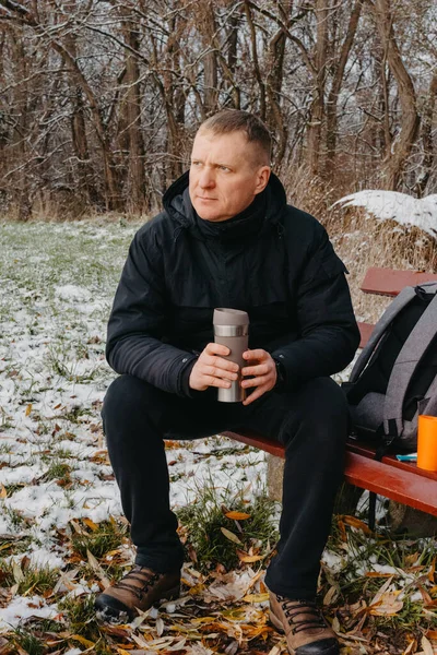 Winter Serenity: 40-Year-Old Man Enjoying Tea on Snow-Covered Bench in Rural Park. Immerse yourself in the tranquil beauty of winter as a 40-year-old man finds solace on a snowy bench in a rural park