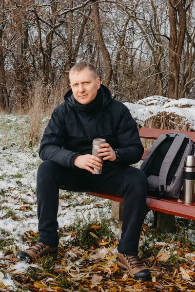 Winter Serenity: 40-Year-Old Man Enjoying Tea on Snow-Covered Bench in Rural Park. Immerse yourself in the tranquil beauty of winter as a 40-year-old man finds solace on a snowy bench in a rural park