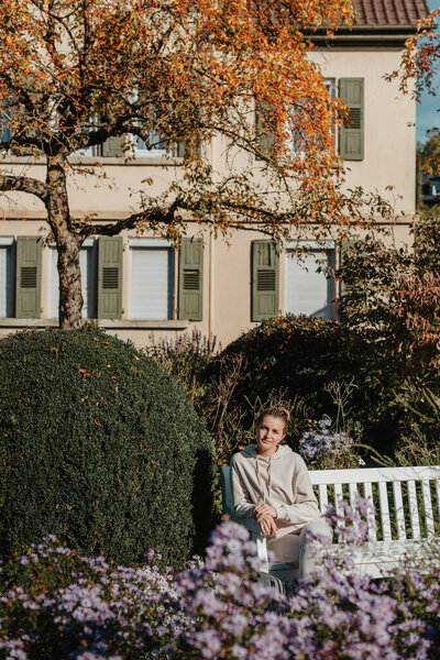 a girl sits on a bench in the park and enjoys the sun. Portrait young adult attractive woman enjoy sitting on bench and relaxing calm carefree rest in city park against green grass and trees on sunny