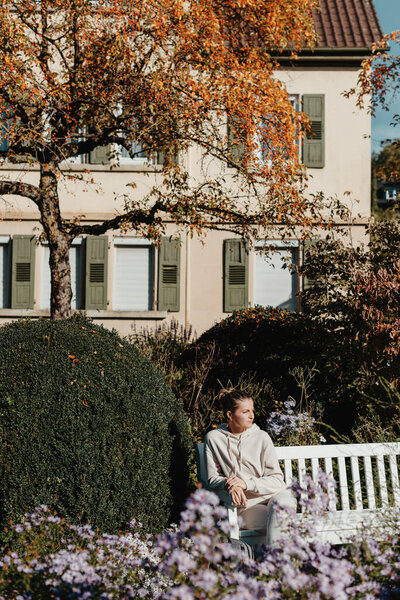a girl sits on a bench in the park and enjoys the sun. Portrait young adult attractive woman enjoy sitting on bench and relaxing calm carefree rest in city park against green grass and trees on sunny
