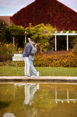 A couple in love hugs on the shore of a city pond in the European town. love story against the backdrop of autumn nature. romantic ambiance, couple goals, outdoor romance, seasonal charm, love in the clipart