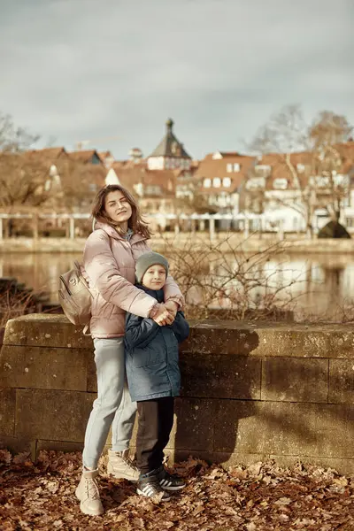 stock image Riverside Family Harmony: Mother, 30 Years Old, and Son - Beautiful 8-Year-Old Boy, Standing by Neckar River and Historic Half-Timbered Town, Bietigheim-Bissingen, Germany, Autumn. Immerse yourself in