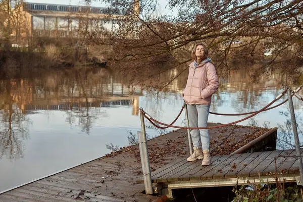 秋天阳光明媚的一天 一位年轻的女子站在岸边看着河水 复制文字空间 旅行照片 穿着保暖衣服的快乐的女游客在河边 图库图片