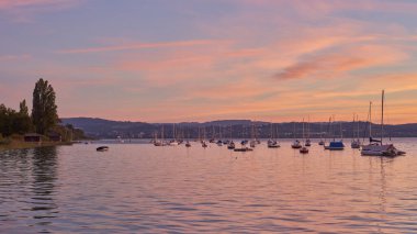 Bodensee Gölü Panorama. Akşam, alacakaranlık, batan güneş, manzara, sakin sular, rıhtımda tekneler ve yatlar, suda yansıyan bulutlar, alacakaranlıkta nehir kenarı.